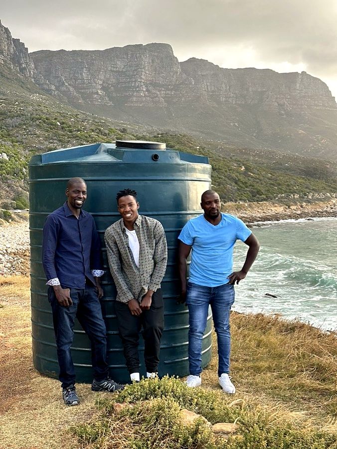 Three men beside a green water tank on the coast