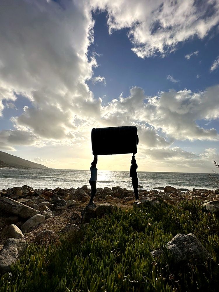 Two people lifting a water tank overhead on the coast at sunset
